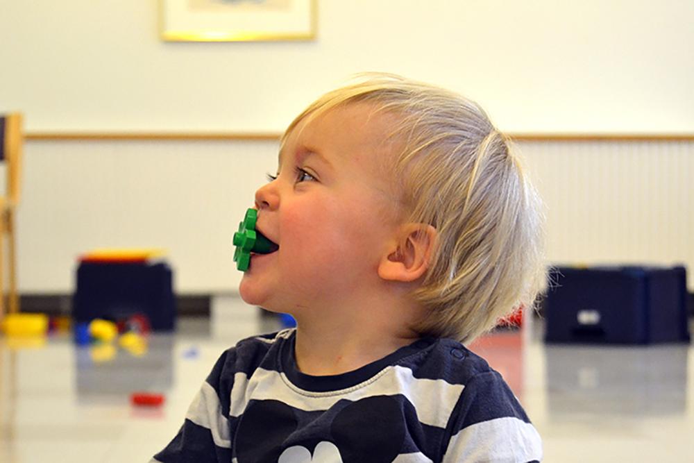 Ett barn i ett- tvåårsåldern klädd i en randig skjorta. Barnet har en grön Duplokloss i munnen.